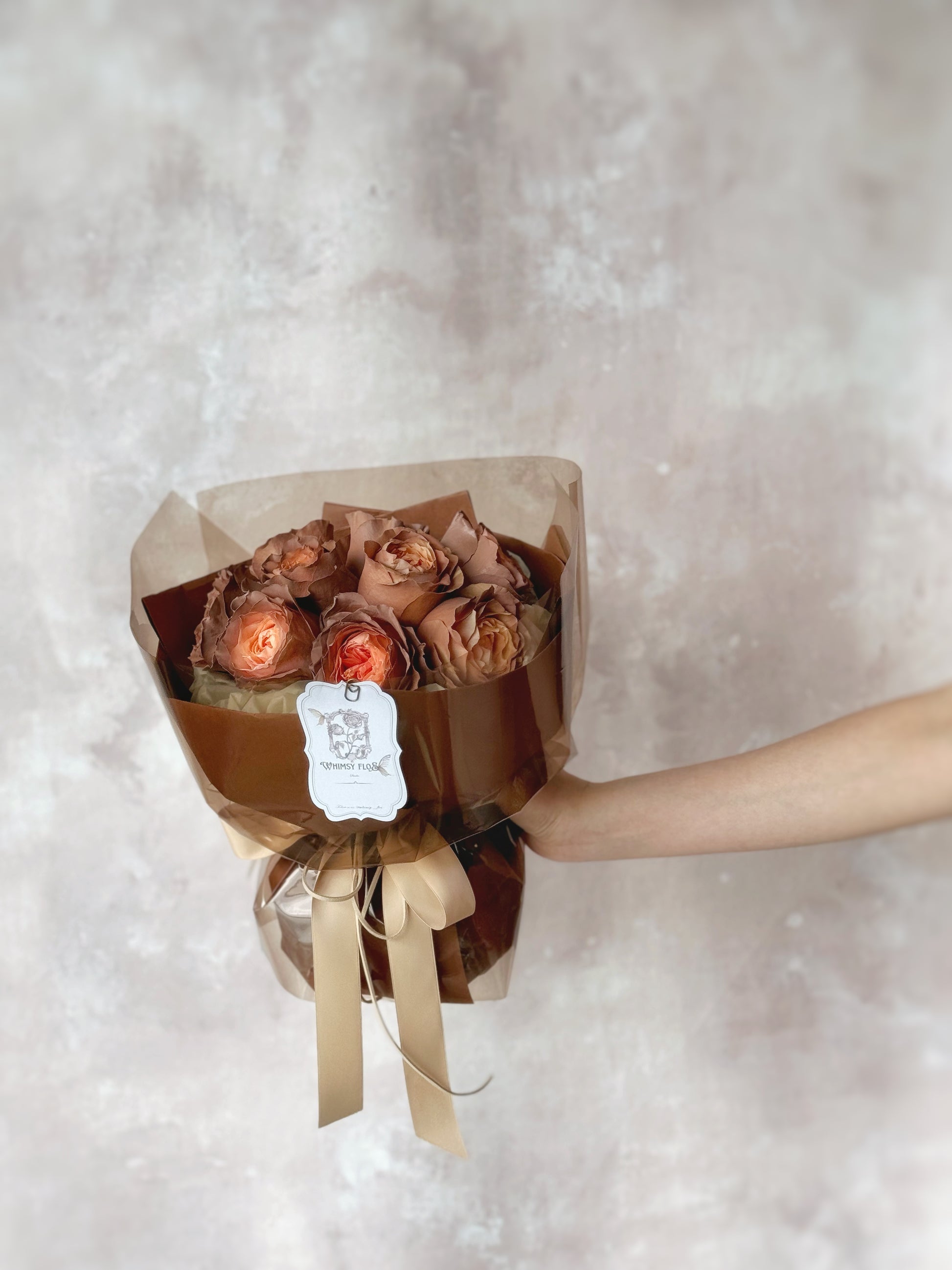 Rose mocha fresh flowers handtied bouquet spray painted rose grand size held in extended arm 手臂前伸持花，仅露出手部与花面，玫瑰柔和色泽与复古包裹成为画面焦点。