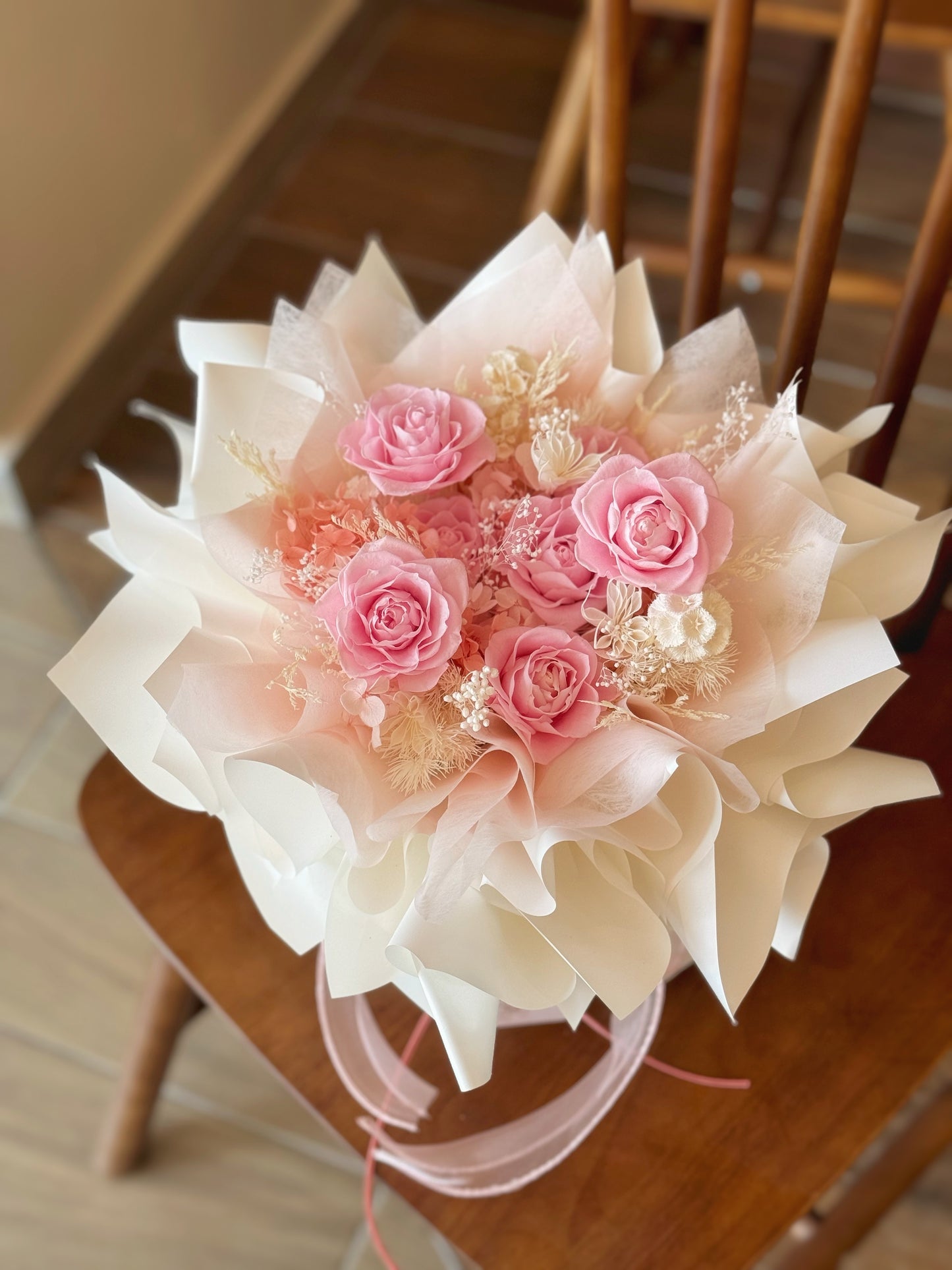 A warm-toned preserved flower arrangement named "Rosie Nest", featuring a charming mix of pastel pink, blush, and nude tones arranged in a round shape.
暖色调的永生花束“Rosie Nest”展示于桌面，融合粉色和裸色花材，营造出温馨舒适的设计。