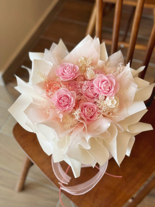 A warm-toned preserved flower arrangement named "Rosie Nest", featuring a charming mix of pastel pink, blush, and nude tones arranged in a round shape.
暖色调的永生花束“Rosie Nest”展示于桌面，融合粉色和裸色花材，营造出温馨舒适的设计。