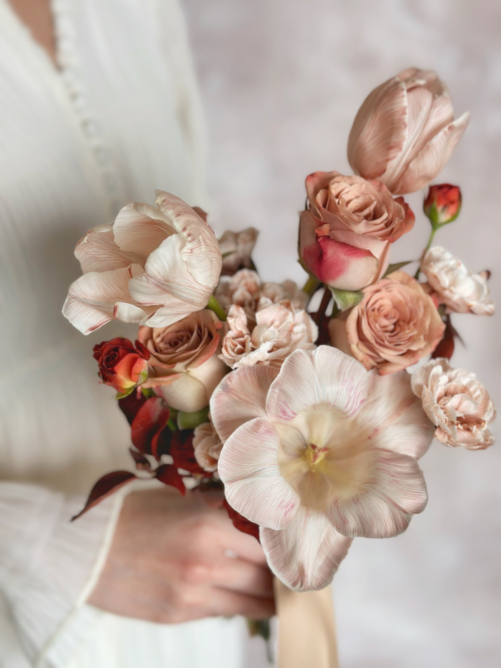 Close up view of stem dyed brownie tulips and cappuccino roses in a bridal bouquet. Elegant tulip arrangement with a mix of blush and deep maroon tones
特写优雅染色大地色郁金香捧花，结合柔粉与深栗色调