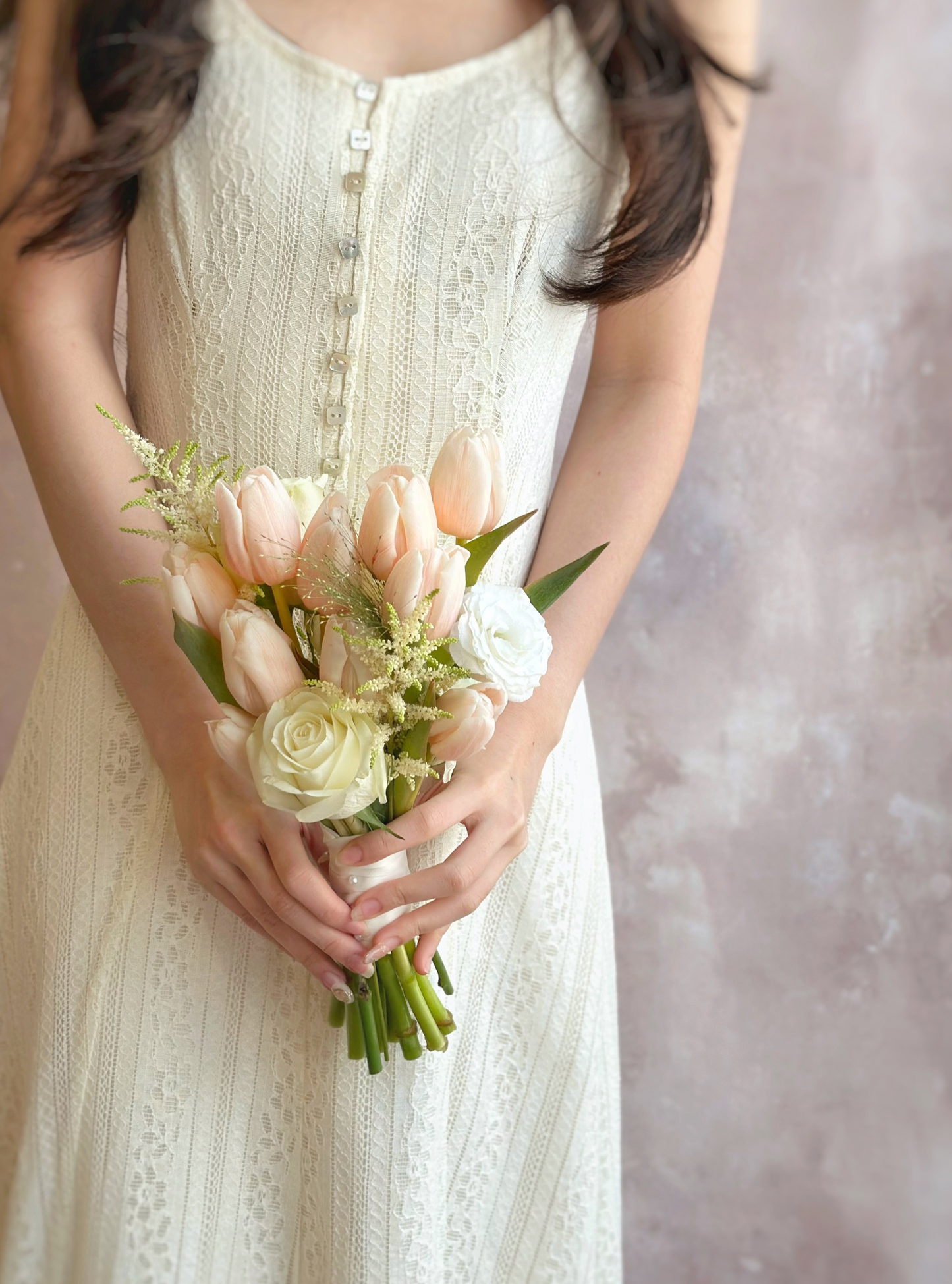 A bride holding the bouquet, its peachy tulips and white blooms complementing her elegant bridal look.
新娘手持捧花，蜜桃色郁金香与白色花朵完美搭配，衬托优雅新娘造型。