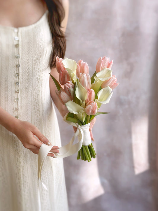 A bride in a minimalist white dress holding a sleek and elegant Korean-style bouquet, with white calla lilies and pink tulips, embodying simplicity and sophistication.
身穿极简白色婚纱的新娘手持优雅韩式捧花，完美诠释简约与高雅。