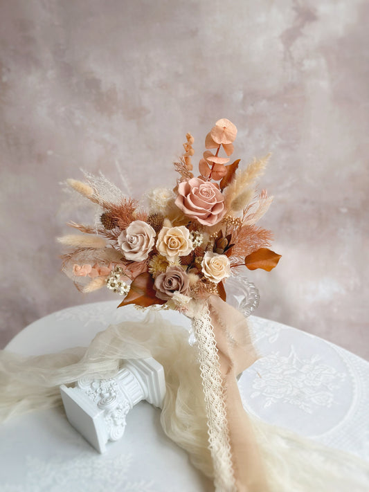 A sophisticated preserved bridal bouquet in warm earthy tones, featuring an elegant mix of neutral and fall-inspired hues.
一款典雅的暖色调永生花新娘捧花，融合了中性色与秋日灵感色调。