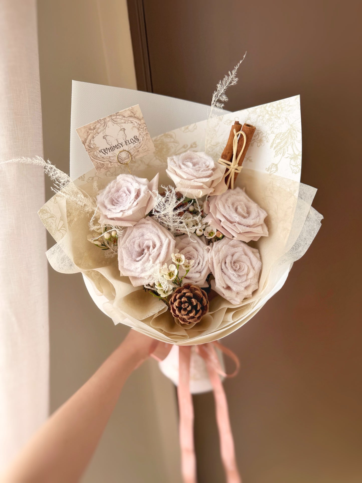 Close-up of snow-kissed mauve manta roses paired with natural pinecones and cinnamon sticks.
 雪霜质感粉紫玫瑰特写，搭配天然松果和肉桂棒。