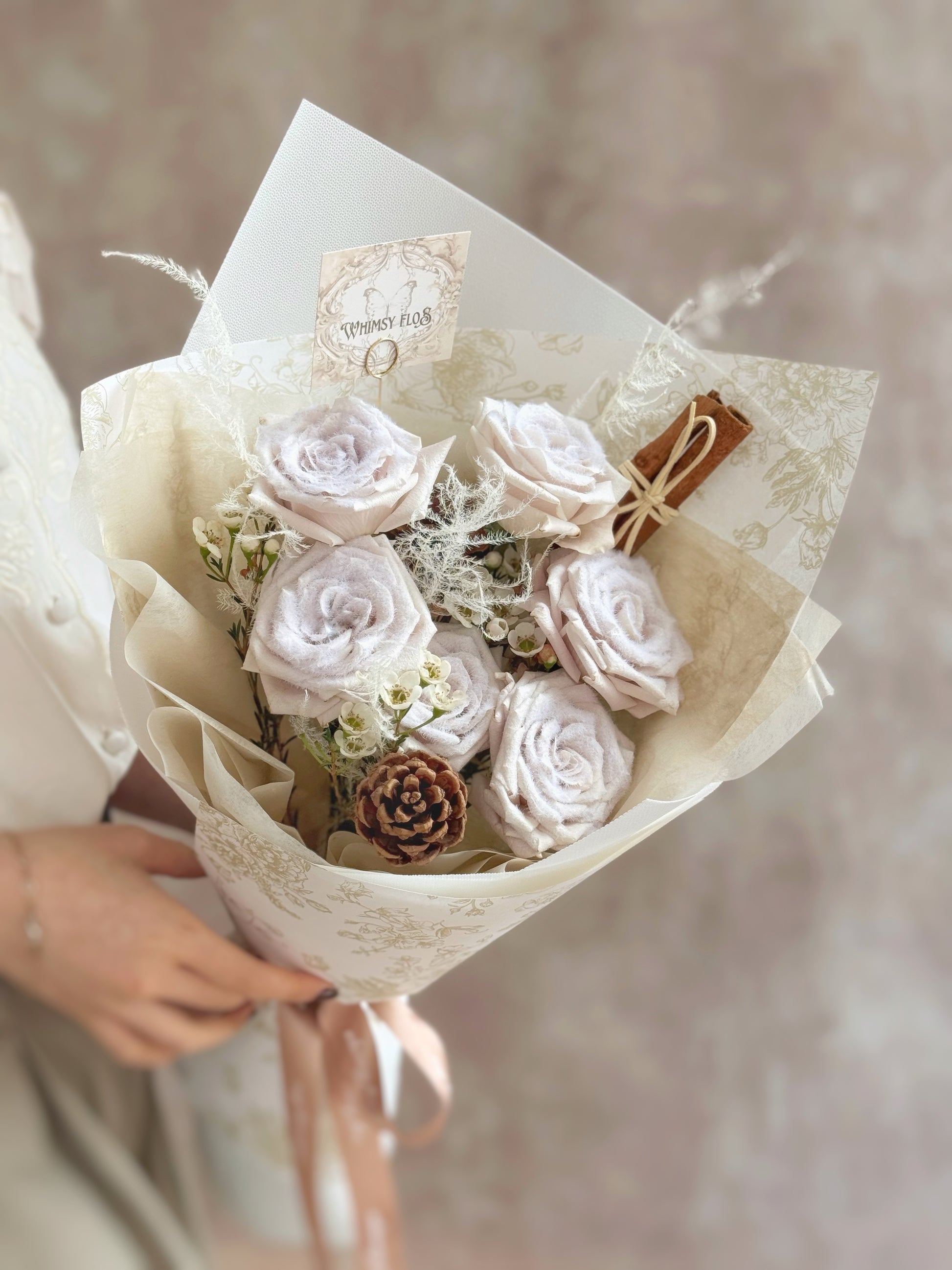 Snow-effect pale mauve manta rose Christmas bouquet styled with pinecones and cinnamon sticks for a soft winter look.
雪霜曼塔玫瑰圣诞花束，全景搭配松果与肉桂，呈现柔和冬季风。