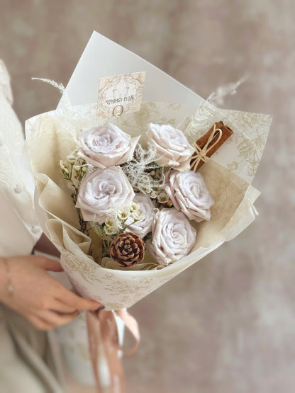 Snow-effect pale mauve manta rose Christmas bouquet styled with pinecones and cinnamon sticks for a soft winter look.
雪霜曼塔玫瑰圣诞花束，全景搭配松果与肉桂，呈现柔和冬季风。