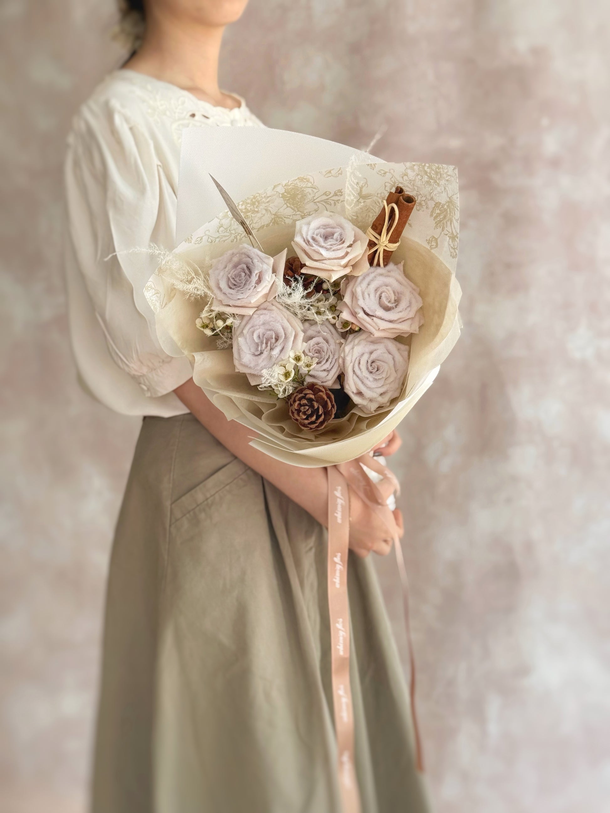 Model presenting a handcrafted mauve Christmas bouquet with snow-effect roses, pinecones, and cinnamon sticks, perfect for holiday gifting.
 模特手持手工粉紫圣诞花束，雪霜玫瑰配松果和肉桂棒，适合作为节日礼物