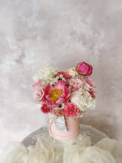 Sunkissed Peony bloom box placed on a table, highlighting the coral sunset peony surrounded by seasonal blooms, arranged beautifully in a compact bloom box.”