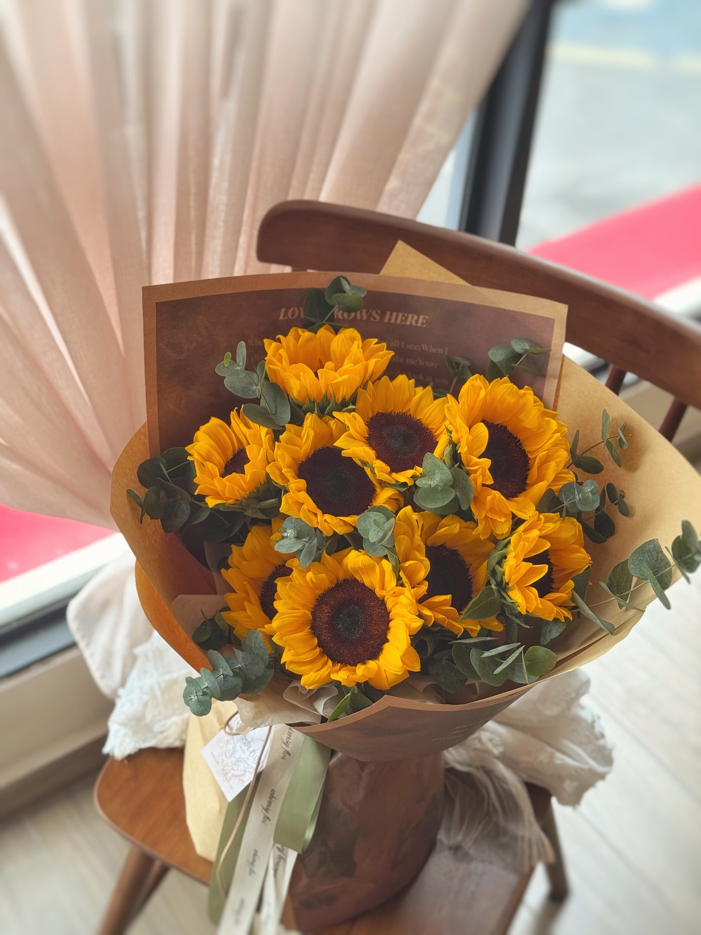 Sunflower and eucalyptus bouquet displayed on a wooden chair, showcasing its earthy kraft wrapping and cheerful aesthetic.
花束摆放于木椅子上，牛皮纸包装自然朴实，整体氛围明快温暖。