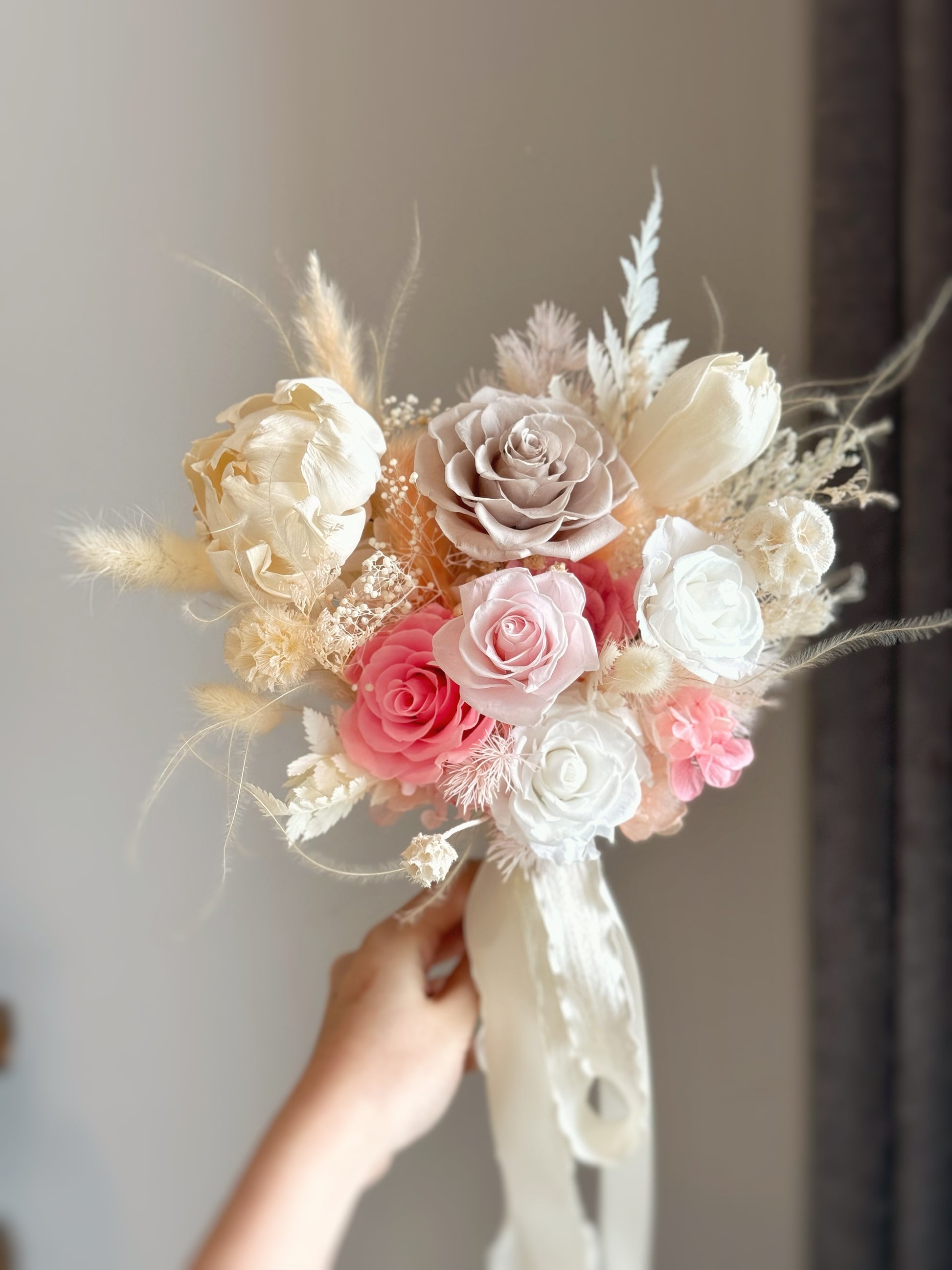 A bride holding the bouquet, its soft nude and pink hues adding a sweet and feminine touch to her wedding look.
新娘手持捧花，裸色与粉色花朵为婚礼造型增添甜美柔和氛围