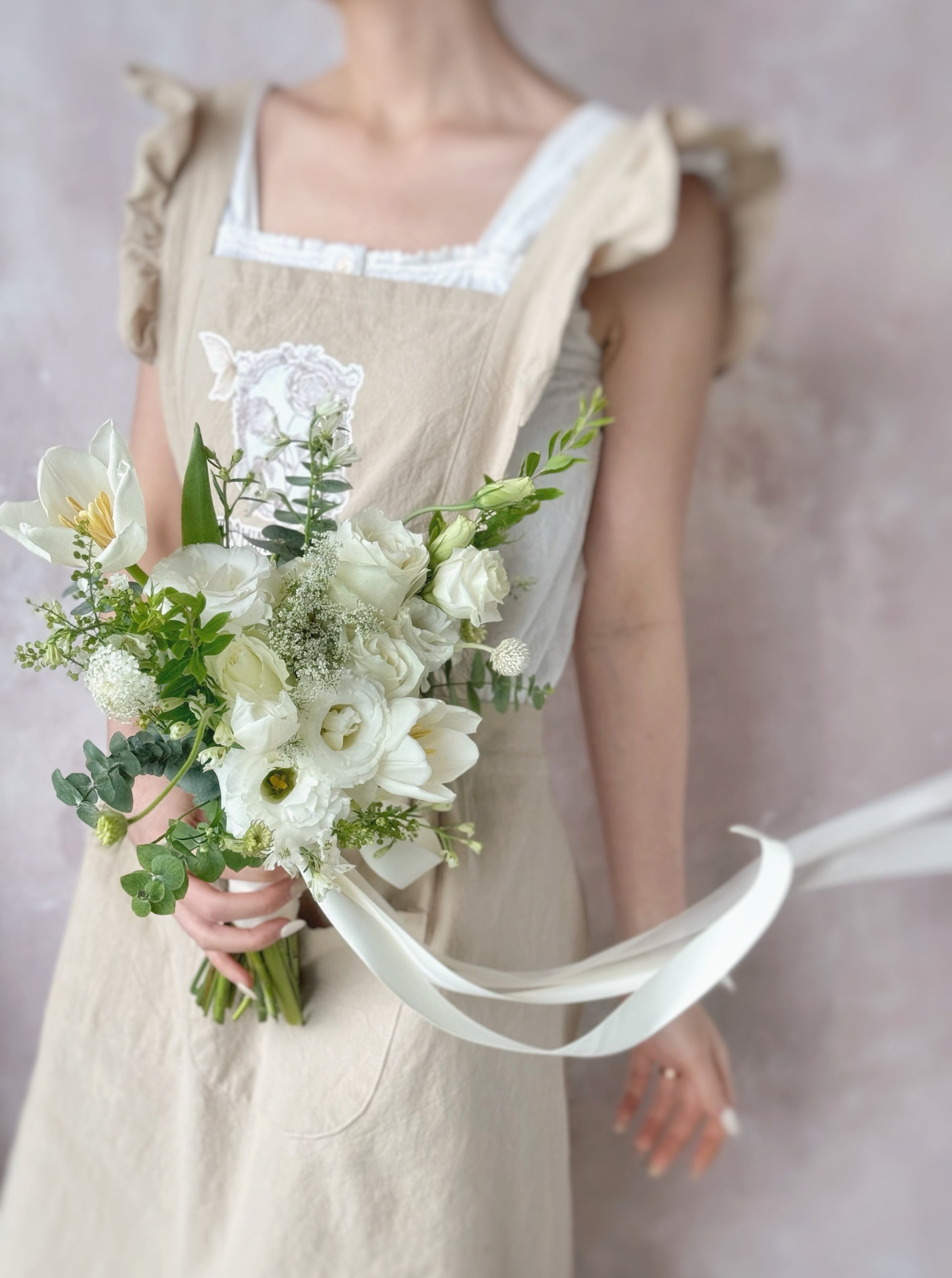 A model holding a graceful arrangement of white flowers and greenery, adding a fresh and elegant touch to any wedding.
新娘手持柔美白色捧花，搭配绿叶，完美演绎经典自然婚礼风格


