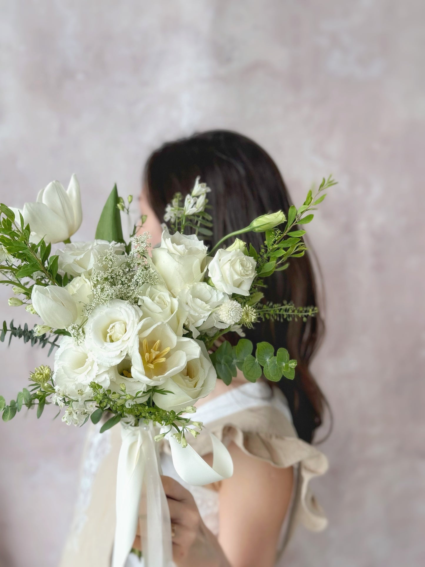 Close-up of a model holding a white bridal bouquet with flowing greenery, capturing a timeless wedding look
白色婚礼捧花的细节特写，展现纯净与清新的美感

