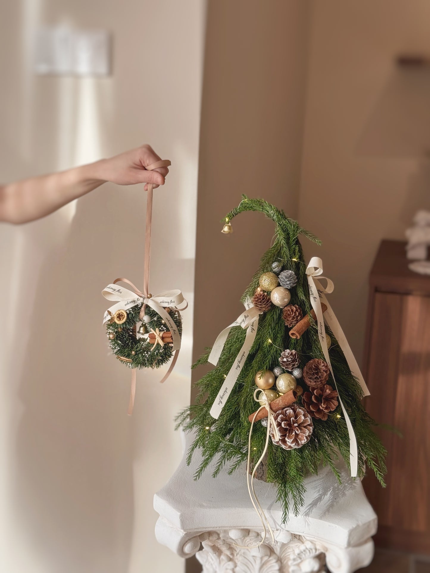 Decorative Nobilis Fir Christmas tree with ornaments and a Mini Christmas wreath ornament on a neutral background