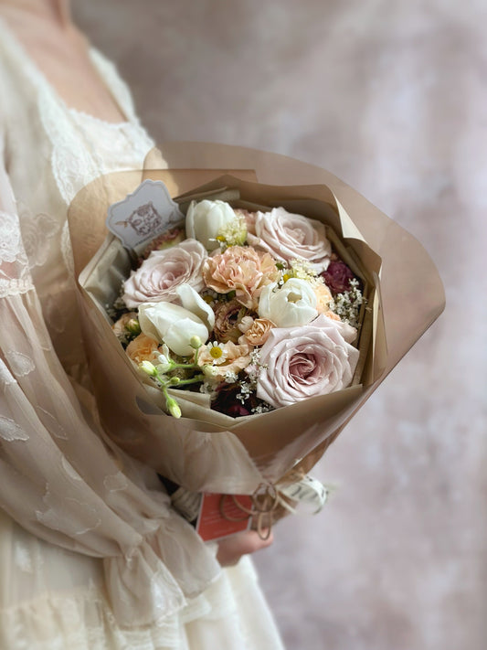 Side angle of the bouquet showing its rounded shape and layered Russian wrapping in muted neutral tones, capturing the vintage-modern blend.

侧面视角展现圆形花束造型与分层俄式包裹设计，低饱和中性色调交织出复古与现代的融合。