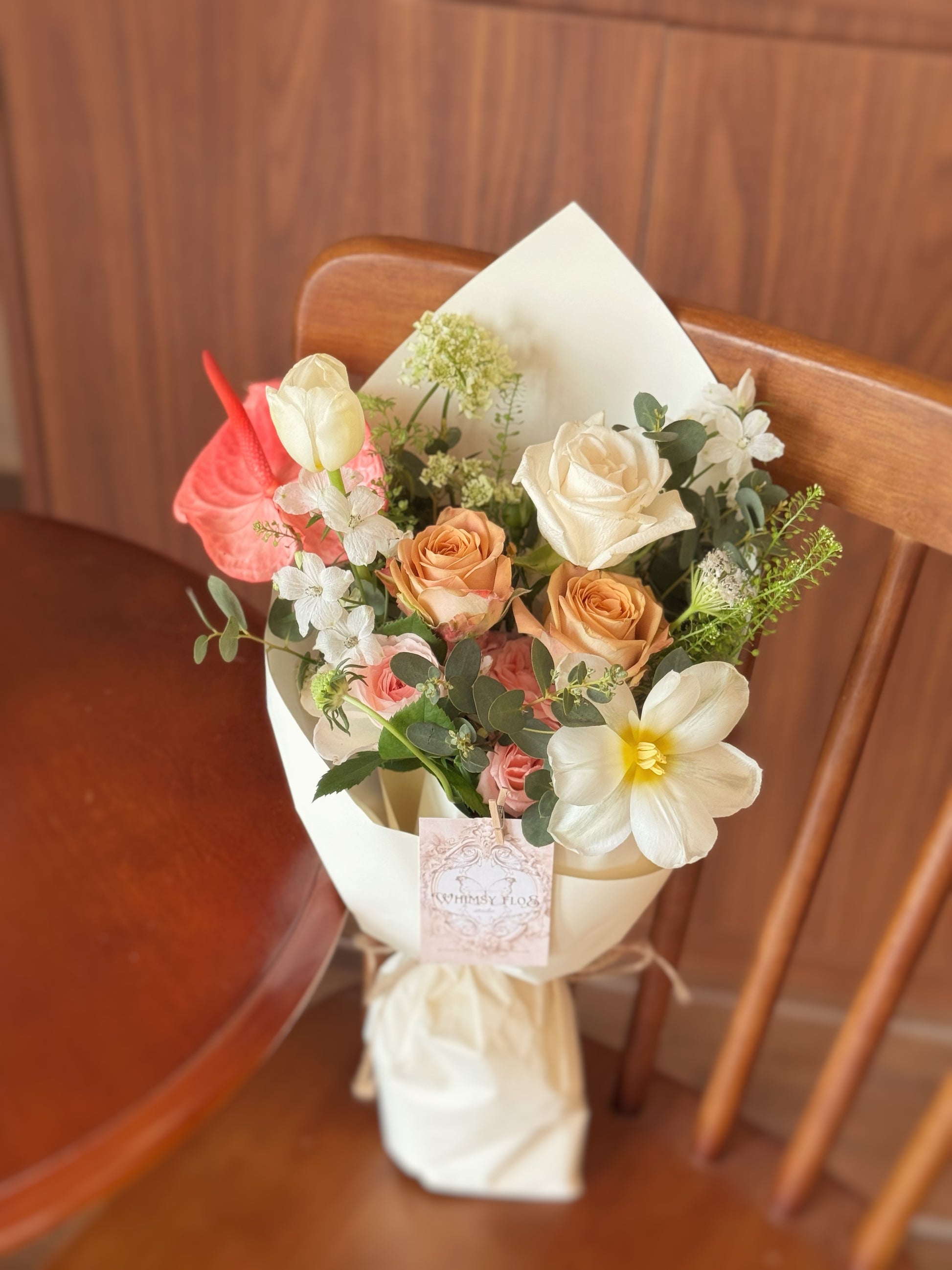 Front view of a premium hand-tied bouquet with tulips, anthurium, roses, and lush greenery, wrapped simply and styled for easy vase placement.
正面展示高级感手绑花束，融合郁金香、火鹤花、玫瑰与绿植配材，简约包裹，方便直接插瓶摆放。