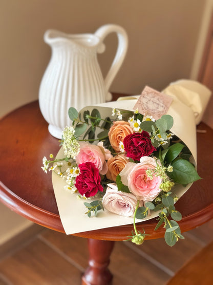 Top-down view of mixed-color roses and seasonal accents arranged in a soft round form — bouquet may vary with seasonal availability.
俯视图展示多色玫瑰与季节性花材的组合，圆润造型，每束因应时花材略有不同