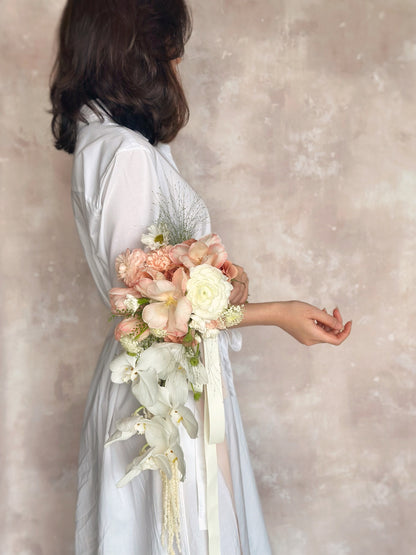 A graceful, cascading bouquet featuring dreamy peach-toned florals for a timeless wedding look
以梦幻蜜桃色花卉打造的优雅瀑布式捧花，尽显经典新娘气质