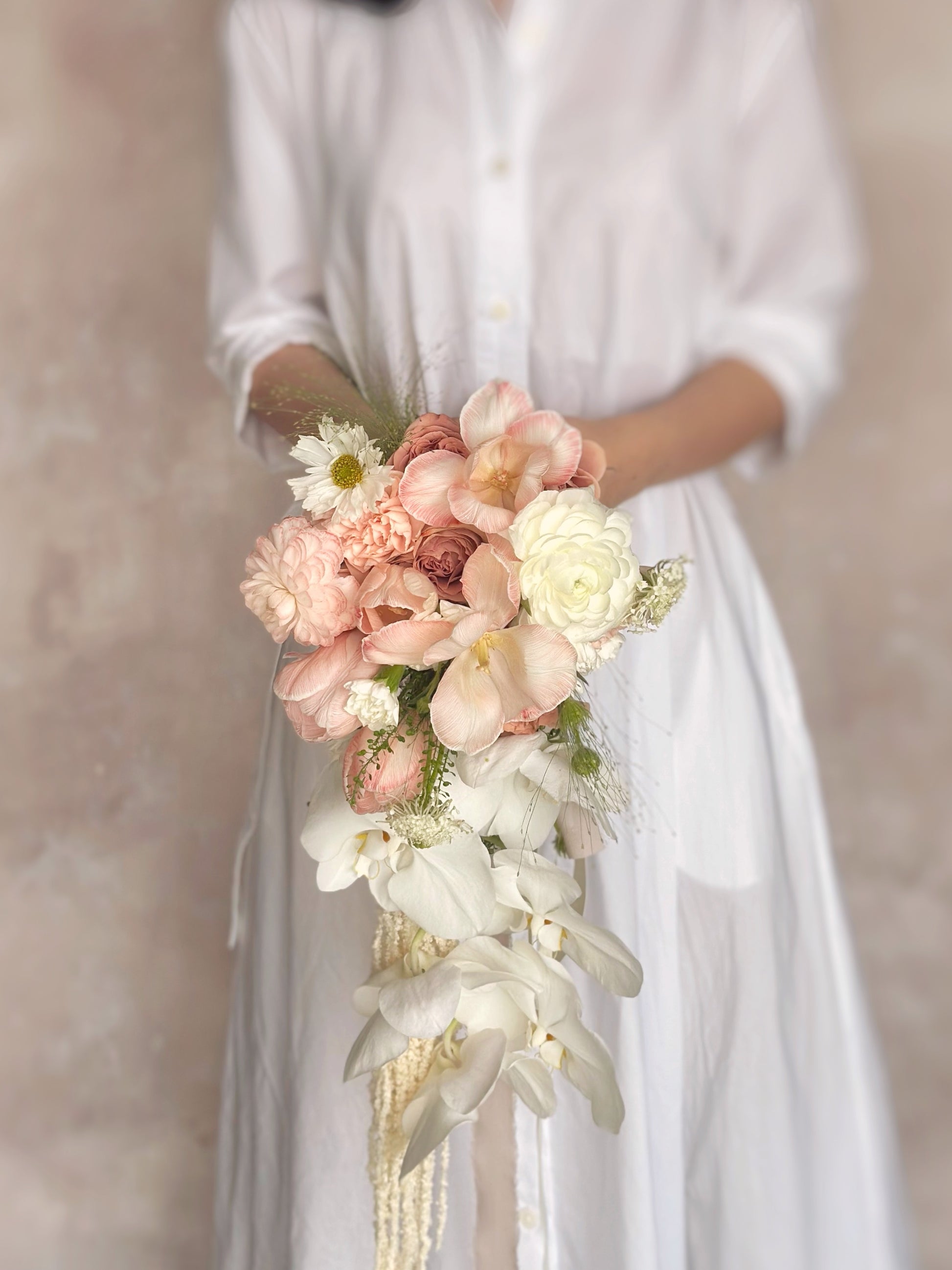 A cascading bouquet in warm peach tones, complementing a romantic bridal ensemble
温暖蜜桃粉色瀑布式捧花，与新娘造型完美融合